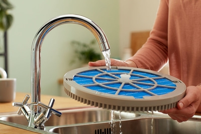 Person wäscht Filter unter fließendem Wasser in der Spüle, um ihn zu reinigen.