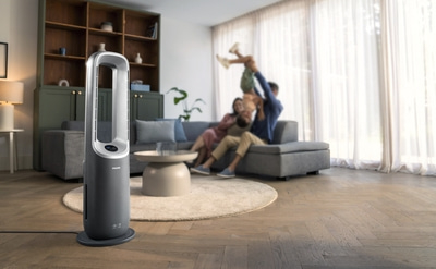 Familie spielt im Wohnzimmer mit Ventilator. Grauer Ventilator, Familie auf Sofa.