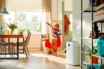 Kind und Hund als Superhelden mit Luftreiniger im Wohnzimmer